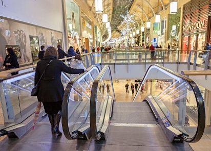 An image of a woman leisurely strolling down an escalator in a populated shopping mall